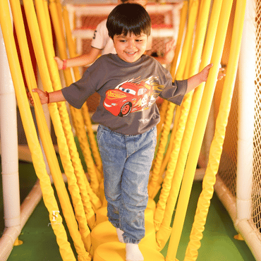 Child walking through a colourful rope bridge at Wooray Delhi indoor play area.