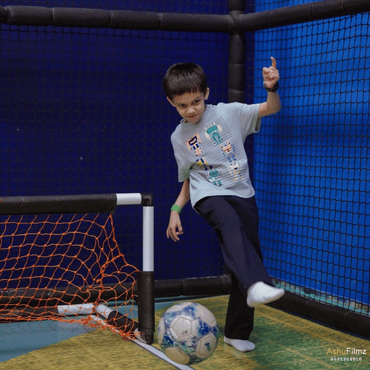 Boy playing football in an indoor sports play area.