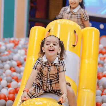 Girl enjoying a yellow indoor slide surrounded by colourful play equipment.