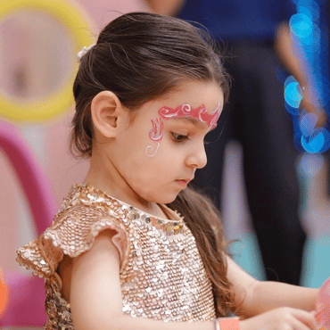 Girl enjoying a face painting activity at an indoor kids play area.
