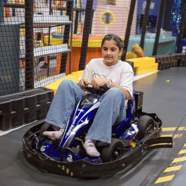 Girl enjoying a blue go-kart ride on an indoor racing track.