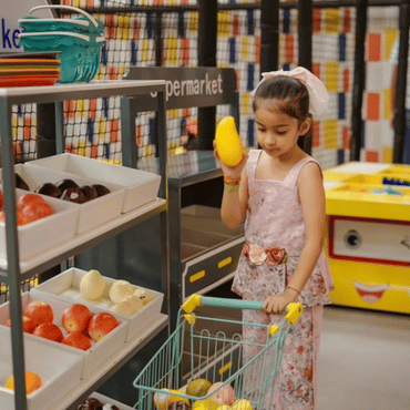 Girl enjoying pretend shopping with a toy cart in a kids play area.
